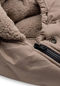 Beige buitenstof met een gestructureerde afwerking, voorzien van een zachte, fluffy voering en een zwarte rits. Opvallende hardware omvat een gouden ooglet.