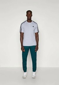 Harmaa lyhythihainen urheilupaita, jossa on mustat raidat olkapäillä, yhdistettynä vihreisiin housuihin, joissa on sivuraidat, ja valkoisiin lenkkareihin.