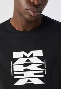 Sort t-skjorte i bomull med et dristig grafisk design i hvitt som inneholder geometriske former og tekst. Rund hals, korte ermer, myk tekstur.