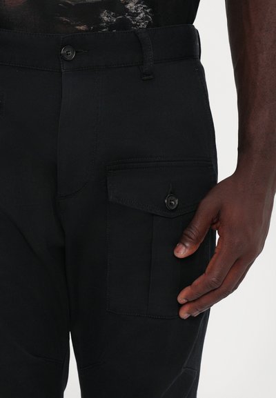 Black cargo pants with a textured finish, featuring a side pocket with a button closure and a visible stitch pattern.