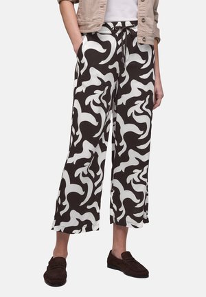 Person iført sort-hvide abstrakt mønstrede vide korte bukser med en beige jakke, hvid top og mørkebrune loafers.