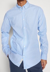  Lichtblauw overhemd met verticale witte en oranje strepen, lange mouwen, button-down kraag en gebogen zoom. Zachte stof textuur.