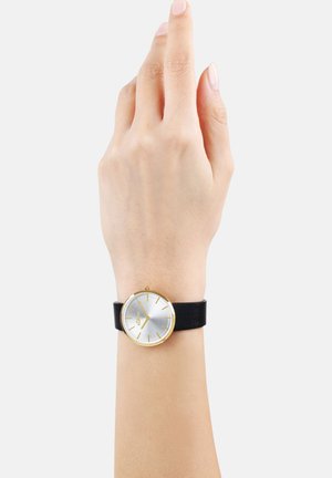 Runde silberne Uhr mit goldenen Akzenten und schwarzem Lederarmband. Sie verfügt über ein minimalistisches Design und dünne Stundenmarkierungen, die an einem Zeiger angezeigt werden.