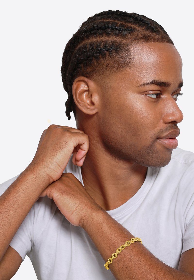Braccialetto in oro sulla wrist, camicia bianca a maniche corte, capelli intrecciati, pelle liscia e profilo laterale del viso.