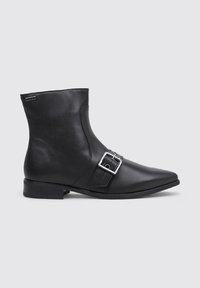 Bottine en cuir noir avec un bout pointu, un talon bas et une bande à boucle en métal argenté à l'avant, sur un fond gris clair uni.
