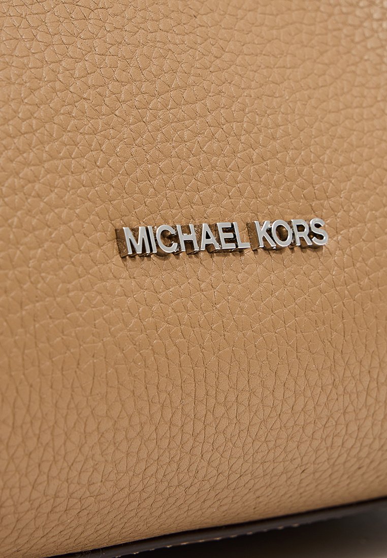 Tan läderhandväska med en strukturerad yta som har en silverfärgad "MICHAEL KORS" logotavla som en framträdande detalj.