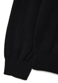 Detail eines schwarzen Strickpullovers mit geripptem Saum und glatter Textur, leicht locker sitzend an der Ärmelaussparung.