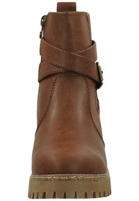 Brązowy skórzany botek sięgający kostki z detalami w formie krzyżowych pasków, bocznym zamkiem błyskawicznym oraz teksturowaną gumową podeszwą. Posiada słupek obcas i dekoracyjną klamrę.