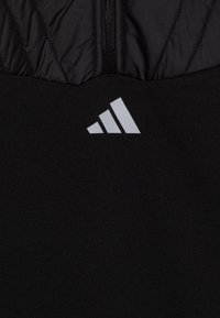Czarny sportowy top z teksturowaną górną częścią i gładkim dolnym panelem. Na przodzie widoczne srebrne logo Adidas.