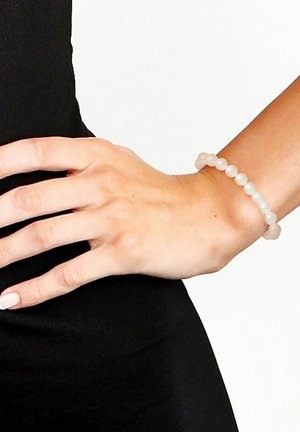 Bracelet élastique composé de perles rondes et lisses de couleur blanche laiteuse, étroitement enfilées ensemble, porté sur un poignet avec un fond noir.