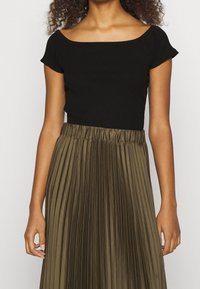 Mustapaitainen, ribatteinen lyhythihainen paita yhdistettynä laskostettuun oliivinvihreään hameeseen, jossa on joustava vyötärö ja pehmeä, sileä tekstuuri.