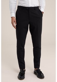 Pantalons noirs ajustés avec une coupe slim, devant plat, poches latérales et une texture lisse, associés à des mocassins noirs et une chemise blanche.