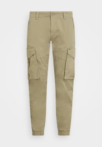 Beige cargobroek met klepzakken op beide dijen, knoop- en ritsluiting, riemlussen en elastische boorden bij de enkels.