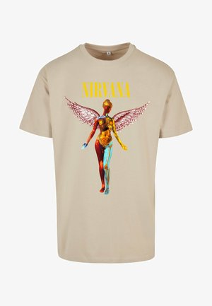 T-shirt di cotone beige con una grafica di una figura anatomica stilizzata dai dettagli colorati e ali d'angelo. Testo: "NIRVANA" in giallo.