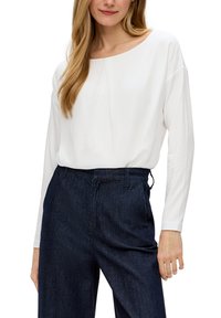Witte blouse met lange mouwen en een ronde halslijn, voorzien van een voorplooitje. Gekombineerd met donkerblauwe high-waisted jeans. Zachte, gladde textuur.