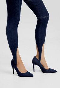 Laivansiniset korkokengät, joissa on terävä kärki. Yhdistetty tummansinisiin denim-legginseihin, joissa on sivurei'itykset, mikä korostaa tyylikkäitä tekstuureja.