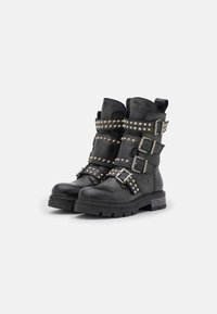 Botas de cuero negras hasta el tobillo con múltiples hebillas de plata, detalles con tachuelas y una suela gruesa y resistente. Incluye un tirador en la parte trasera.