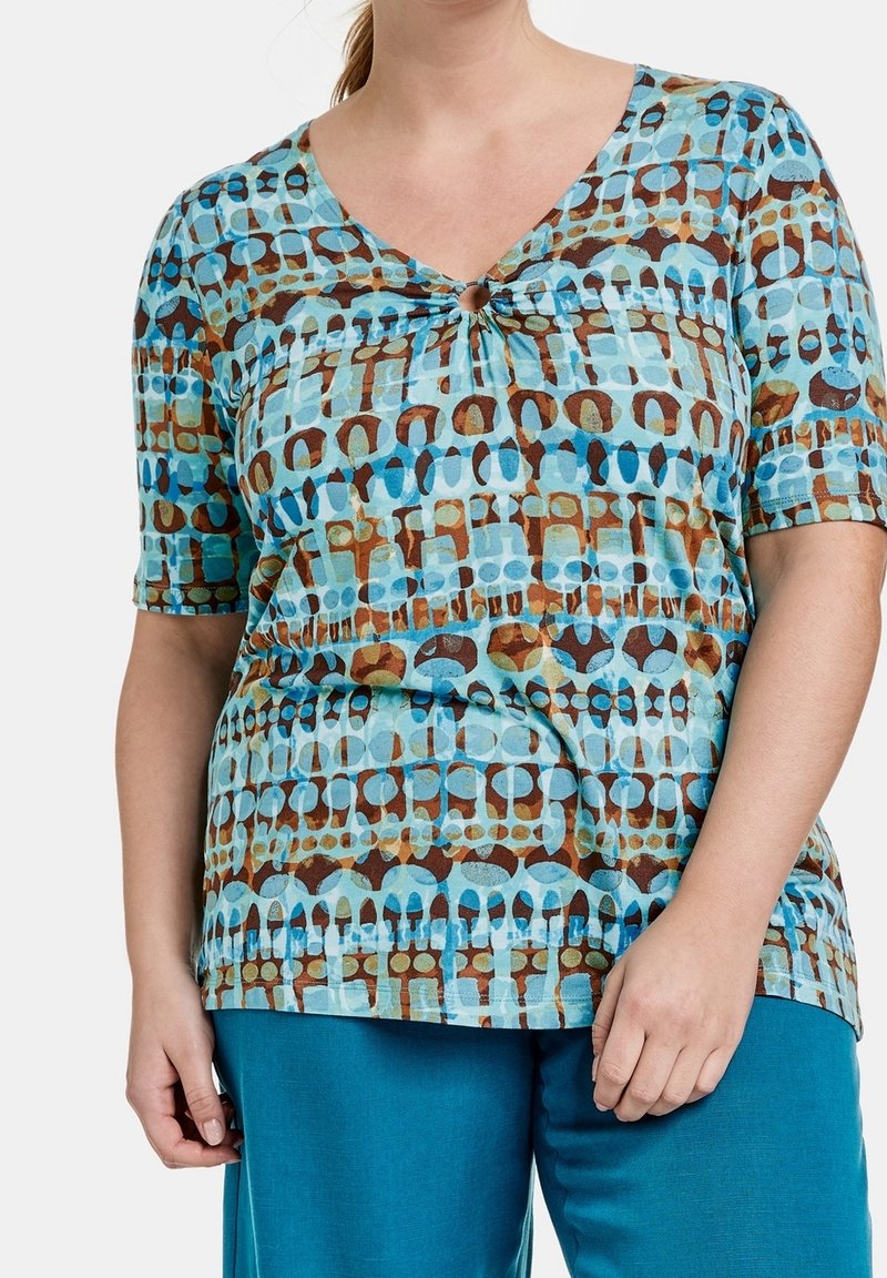 Top a maniche corte in teal con un design a motivi nelle tonalità di blu e marrone, dotato di un dettaglio a chiave sul collo. Tessuto di texture liscia.
