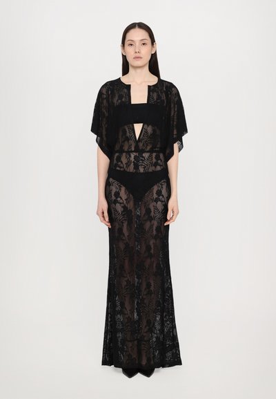 Robe en dentelle noire avec des motifs floraux transparents, corsage ajusté, décolleté en V profond et manches ouvertes, associée à un bas de bikini noir.