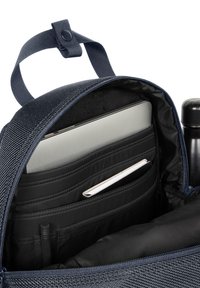Ordinateur portable, carnet, stylo et bouteille d'eau organisés à l'intérieur du compartiment principal d'un sac à dos bleu marine avec fermeture éclair.