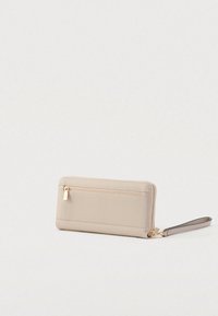 Beige portemonnee met een textuur en een ritssluiting, voorzien van een zak aan de voorkant en een afneembare polsband, afgewerkt met gouden details.
