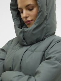 Napihnjena jakna v umirjeni zeleni barvi, s stoječim ovratnikom z kapuco, prešito teksturo, sprednjimi zapahi in minimalističnim dizajnom.