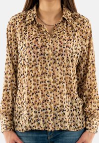 Camicia bottonata in tessuto leggero e stampato con una base beige e macchie multicolori. Maniche lunghe con polsini bottonati.