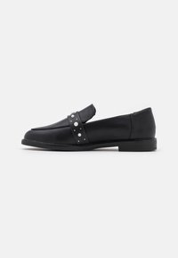 Black leather loafers feature a flat sole, pointed toe, and a decorative strap adorned with faux pearls and studs for added detail.