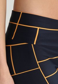 Leggings blu navy con cintura elastica, caratterizzati da un motivo a griglia delineato in arancione. Il tessuto è liscio e elasticizzato.
