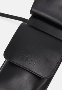 Sac bandoulière en cuir noir avec fermeture à rabat embossée des lettres MSGM, présenté en gros plan.