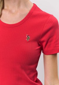 Rotes, geripptes T-Shirt mit rundem Ausschnitt, kurzen Ärmeln und kleinem, auf der Brust gesticktem Detail mit einer Figur.
