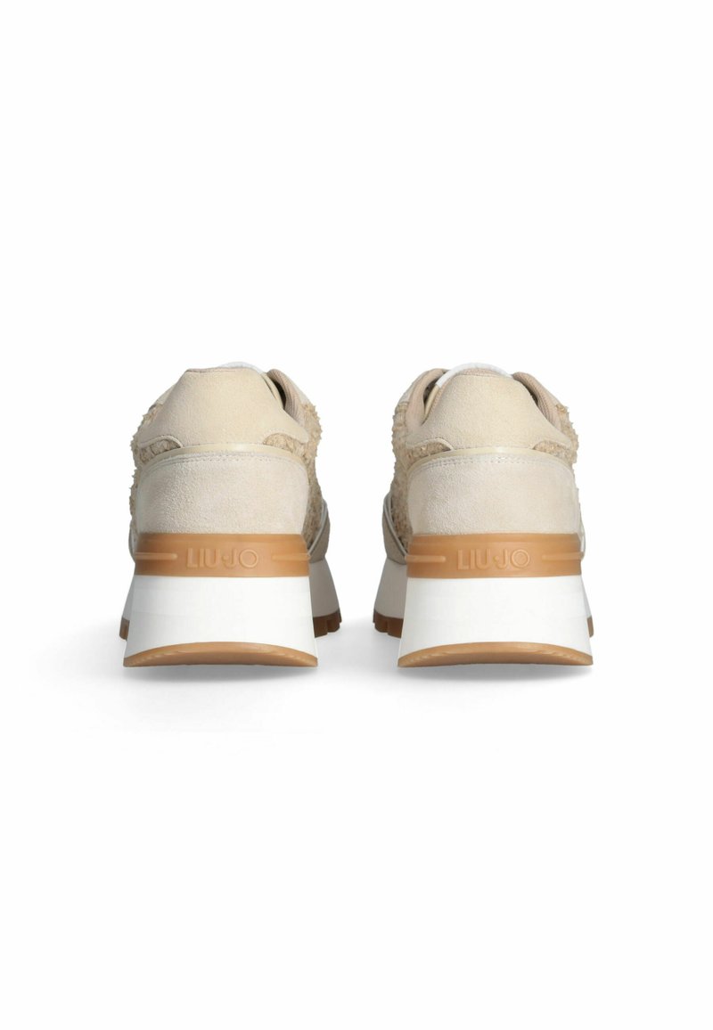 Sneaker beige con una toma superiore testurizzata, dettagli in camoscio e un tallone bianco. Presenta una suola in gomma color nocciola e un logo visibile sul retro.