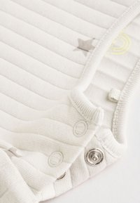 Close-up of white ribbed baby clothing with snap buttons and small printed stars and rainbow details.