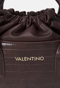 Brun handväska i konstläder med krokodilmönster, med samlad topp, guld "Valentino"-logotyp, slät yta och strukturerad form.