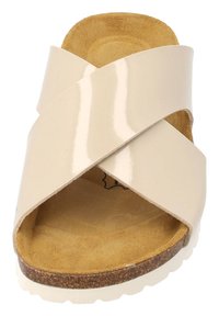 Sandalia de tiras cruzadas beige con acabado brillante, plantilla de suave ante y suela texturizada similar al corcho para mayor agarre y comodidad.