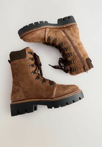 Br�ązowe zamszowe buty z solidną czarną gumową podeszwą, metalowymi oczkami i brązowym sznurowaniem. Zamek błyskawiczny z boku dla łatwego zakładania.