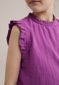 Top viola senza maniche con rifinitura a rouches sulle spalle e tessuto testurizzato. Presenta un collo rotondo e un design morbido e traspirante.