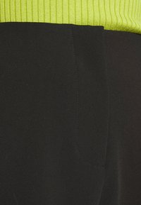 Svart tyg med en ribbad neongrön övre sektion. Har en sidoficka och en slät textur, vilket framhäver en färgblockdesign.