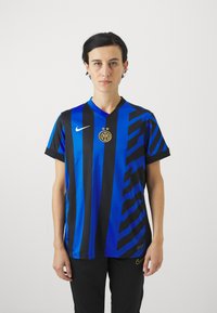 Sininen ja musta raidallinen jalkapallosydäntoppi, jossa on V-kaulus, kultainen seuran logo ja Nike-merkki rinnassa. Sujuva kankaan rakenne.