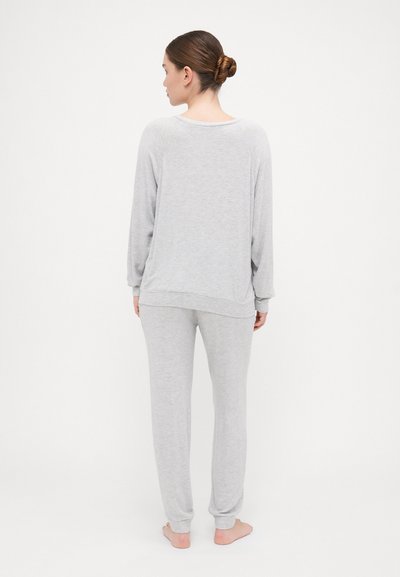 O conjunto de roupa de estar cinza claro inclui uma blusa de manga longa de corte amplo e calças assortidas com punhos canelados. Tecido suave com uma textura lisa.