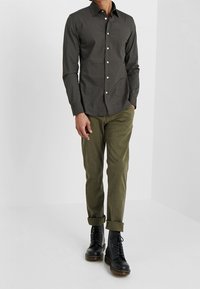 Donkergrijze getailleerde overhemd met een klassieke kraag, gecombineerd met lichtgroene chinos en zwarte enkellaarzen.