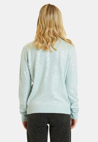 Jasnoniebieski sweter z cekinami o miękkiej teksturze, z prążkowanymi mankietami i dołem. Tylny widok ukazuje błyszczący efekt cekinów.