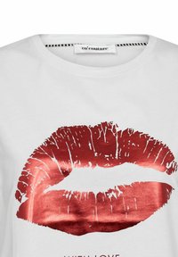 T-shirt en coton blanc avec une grande empreinte de baiser métallique rouge sur le devant, accompagnée du texte "AVEC AMOUR" en dessous du design.