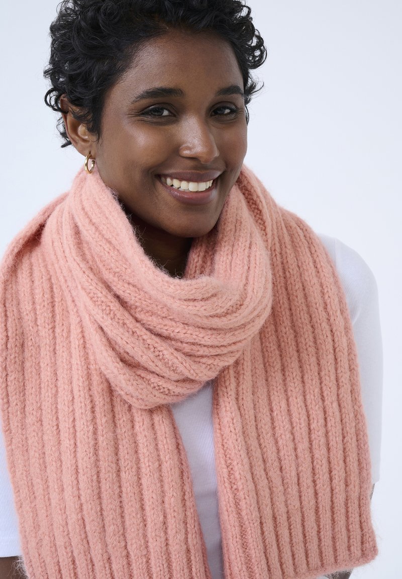 Różowy, prążkowany szalik z miękkiego, teksturowanego materiału, noszony luźno wokół szyi, o delikatnym, ciepłym wyglądzie.
