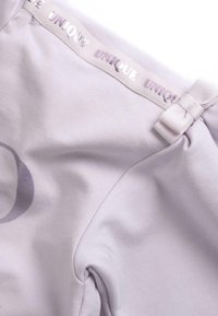 Haut en jersey lilas avec un motif graphique subtil, comprenant un bandeau élastique avec logo et un détail de nœud au niveau du col.