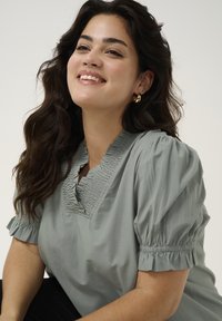 Lichtgroene blouse met pofmouwen, gerimpelde halslijn en geraffineerde accenten. Soepele stof met een relaxte pasvorm.