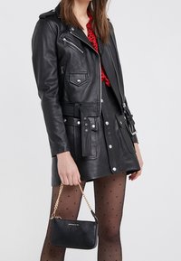 Chaqueta de motorista de cuero negro con herrajes plateados, bolsillos con cremallera y cintura con cinturón, combinada con una falda negra con lunares y un bolso pequeño.