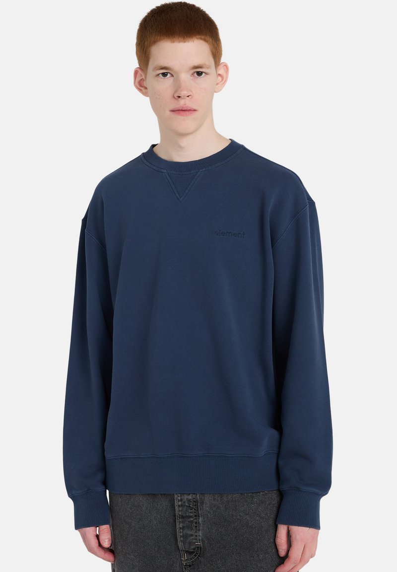 Sudadera azul marino con cuello redondo, confeccionada en tela suave, con hombros caídos, puños acanalados y un pequeño logo en el pecho.