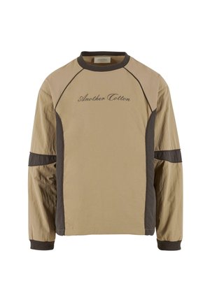 Beige long-sleeve top with dark brown accents, featuring raglan sleeves and embroidered "Another Cotton" text on the front. Smooth texture.