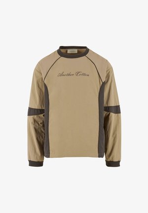 Beige hosszú ujjú felső sötétbarna részletekkel, raglán ujjal, az elején hímzett "Another Cotton" felirattal. Sima текстúra.